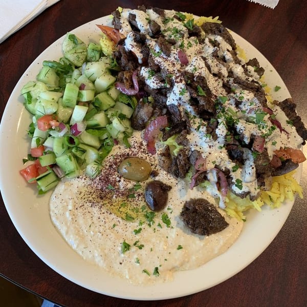 A Mediterranean platter with shawarma, rice, hummus, cucumber salad, and olives.