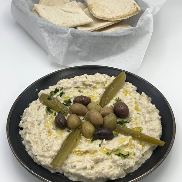 Creamy baba ghanoush topped with olives, pickles, and parsley, served with pita bread.