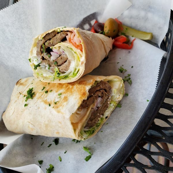 Two halves of a Falafel Hut gyro wrap with meat, lettuce, and sauce, served with pickled vegetables.