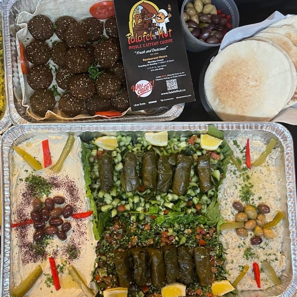 A catering spread from Falafel Hut featuring falafel, pita, hummus, baba ghanoush, tabbouleh, and stuffed grape leaves.